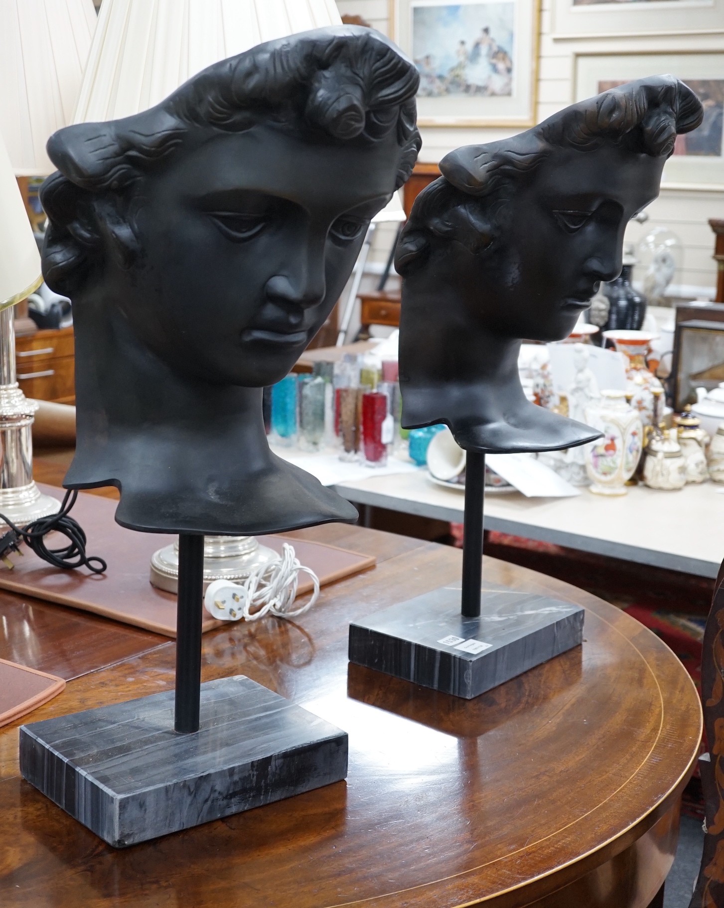 A pair of bronze masks of youths, raised on marble plinths,78cms high